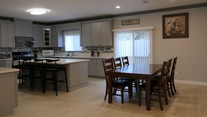 A modern kitchen with grey cabinets, a central island with bar stools, a dining table with chairs, and a 'WELCOME' sign on the wall. - * Living Large * Newly Built * Disneyland & Beaches (Midway City)