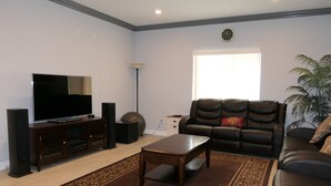 A living room with a flat-screen TV, speakers, a leather sofa, and a patterned rug. - * Living Large * Newly Built * Disneyland & Beaches (Midway City)