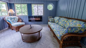 Quarto com paredes azuis, um sofá de vime, uma poltrona de vime, uma mesa redonda e uma lareira.
