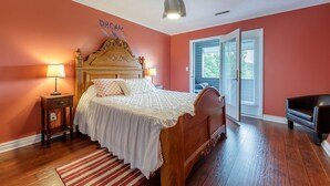 Quarto com cama de madeira, duas mesas de cabeceira com luminárias, parede vermelha e porta que dá para o exterior.