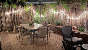 An outdoor patio area with a round table and chairs, a large umbrella, and string lights. - Favorite Downtown Adorable Adobe ~ 10 min walk to Plaza (Santa Fe)