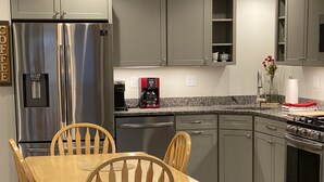 Una cocina moderna con armarios grises, un refrigerador de acero inoxidable, una cafetera y una mesa de comedor con sillas de madera.