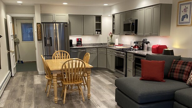 Una cocina moderna con gabinetes grises, electrodomésticos de acero inoxidable y una zona de comedor con sillas y una mesa de madera.