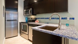 Une cuisine moderne avec des meubles de couleur sombre, des appareils en acier inoxydable, un plan de travail à motifs bleus et blancs, et un évier.