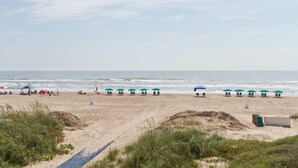 Une plage bordée de rangées de parasols et de chaises de plage, un sentier sablonneux et l’océan en arrière-plan.