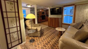 Een woonkamer met een bank, een stoel, een lamp, een televisie en een kamerbreed tapijt met een patroon.