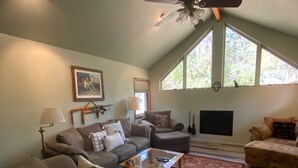 A spacious living room with a high ceiling, a ceiling fan, a large window, and a fireplace. - Escape to Cool Twin Pines! (Pine)