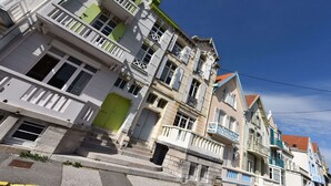 A row of multi-story buildings with balconies, a green door, and a clear blue sky. - Charming Modern cosy Cottage -50m2- (Bourbourg)