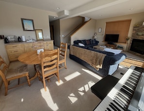 Een woonkamer met een bank, een eettafel met stoelen, een piano, een televisie en een open haard.