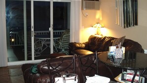 Ett vardagsrum med en brun lädersoffa, ett soffbord i glas och en lampa. Det finns en skjutdörr i glas som leder ut till en uteplats.