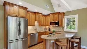 Una cocina con armarios de madera, electrodomésticos de acero inoxidable y una isla de granito con taburetes de bar.