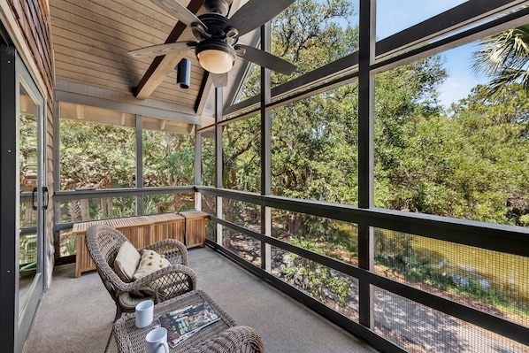 A balcony with wicker furniture, a ceiling fan, and a view of trees.