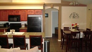 Cocina compacta con armarios de madera, un refrigerador negro y un comedor con sillas y mesa de madera.