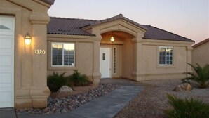Una casa residencial con fachada color beige, techo de tejas y el número 1320 en la pared.