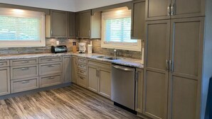 Una cocina con muebles de madera, lavavajillas, microondas y ventana con persianas.