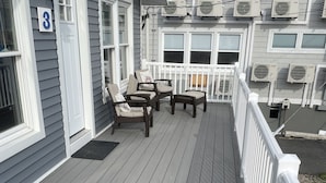 A wooden deck with outdoor furniture, a white railing, and air conditioning units on the building.