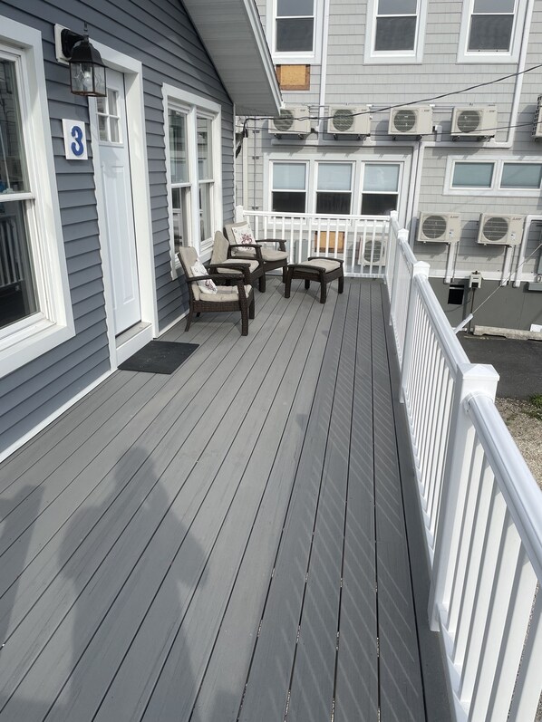 A wooden deck with outdoor furniture, a white railing, and air conditioning units on the building.