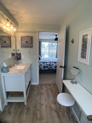 A bathroom with a sink, mirror, and toilet. There is a window with a view of a balcony. - The Beach Barn - Waterfront Cottage on Case Inlet - Kayaks, Beach, Stunning View (Allyn)