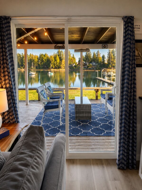 A room with a view of a lake, a sofa, a table, and a chair.