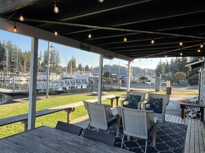 An outdoor patio with wicker furniture and a view of a marina. - The Beach Barn - Waterfront Cottage on Case Inlet - Kayaks, Beach, Stunning View (Allyn)