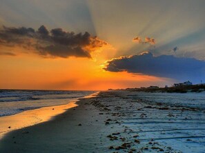 Una playa con un atardecer, mar tranquilo y una costa distante con edificios.