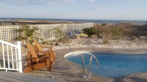 Ein Poolbereich mit Holzterrasse, weißem Zaun und Blick auf den Strand.