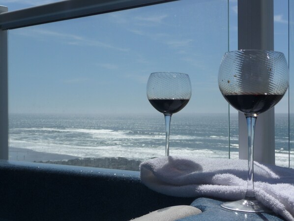 Two wine glasses on a windowsill with a view of the ocean.