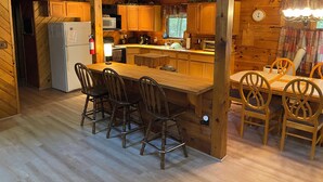 Een houten keuken in chaletstijl met een centraal eiland, houten stoelen en een koelkast.