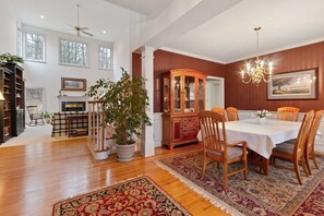 A spacious living room with hardwood floors, a fireplace, a dining area with a table and chairs, and a large potted plant.