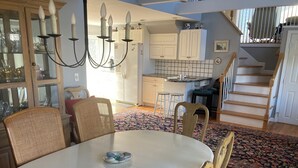 Un espace repas comprenant une table ronde, des chaises et un lustre. Un escalier mène à un niveau supérieur.