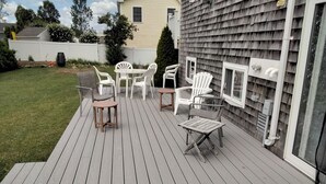 Une terrasse dotée de mobilier d’extérieur, comprenant des chaises et des tables, attenante à une maison avec une fenêtre et une cheminée.