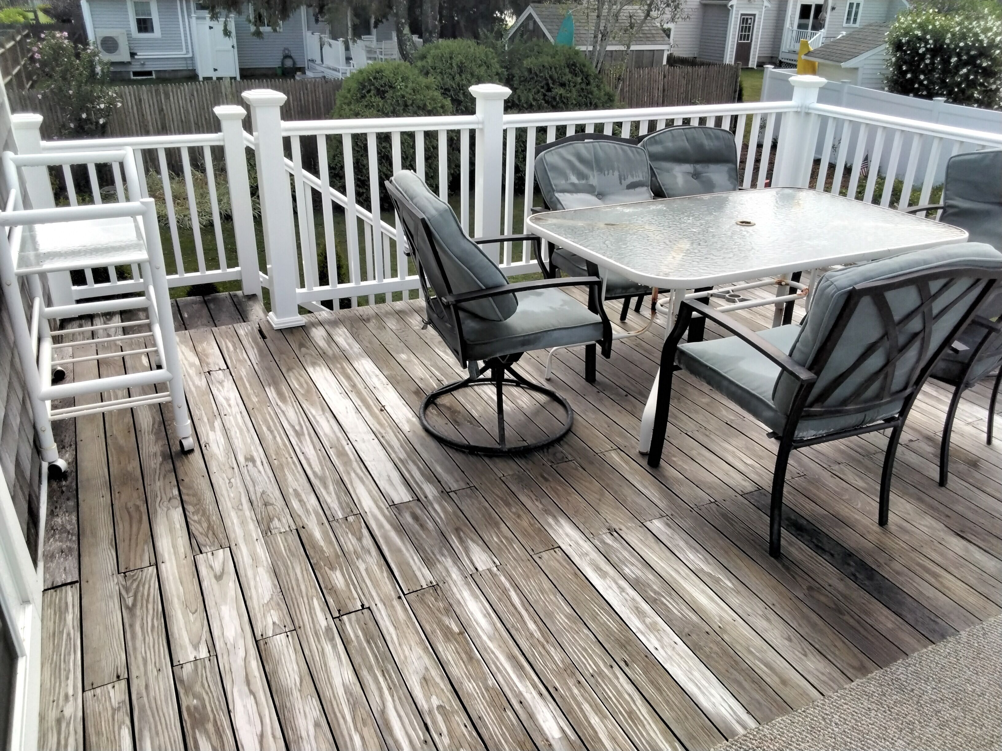 A wooden deck with a table and chairs, surrounded by a white fence.