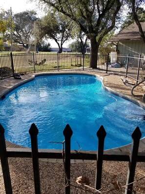 A swimming pool with a surrounding fence, trees, and a building in the background. - Private Pool House With A View (Lago Vista)