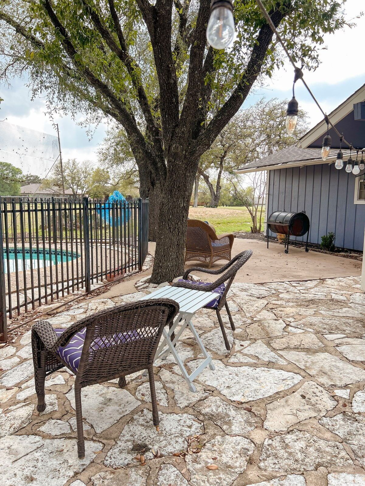 Un patio con mobiliario de mimbre, suelo de piedra y una piscina al fondo.