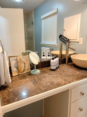 Une salle de bain avec un comptoir en marbre, un meuble-lavabo avec un évier, un miroir et des articles de toilette.