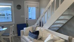 A modern living room with a white sofa, a marble coffee table, a white staircase, and a view through a window. - PERFECT, BEAUTIFULLY NEWLY DESIGNED 1,000 FT. MONTAUK OCEANFRT 3-LEVEL TOWNHOUSE (Montauk)