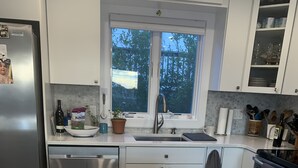 A modern kitchen with a white marble countertop, stainless steel appliances, and wooden stools. - PERFECT, BEAUTIFULLY NEWLY DESIGNED 1,000 FT. MONTAUK OCEANFRT 3-LEVEL TOWNHOUSE (Montauk)