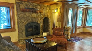A cozy living room with a stone fireplace, wooden furniture, and large windows.