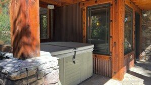 A wooden cabin with a stone foundation, a hot tub, and a large window.