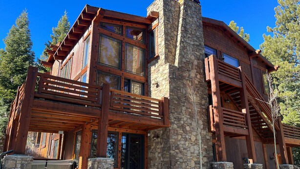A log cabin with a stone chimney, wooden balconies, and a stone foundation.