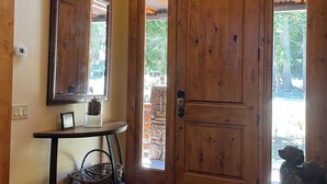 A wooden front door with a glass panel, a wall-mounted mirror, a small table with a basket, and a stone wall visible through the door.