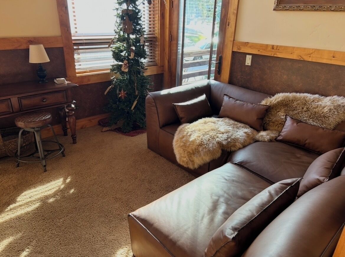 Un salon chaleureux avec un canapé en cuir marron, un petit bureau en bois et un sapin de Noël.