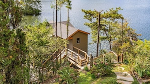A cabin with a wooden deck and stairs leading to a dock by a lake, surrounded by trees. - Lake Summit Estate.  Directly On The Water! (Zirconia)