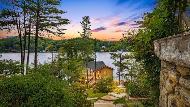 A lakeside cabin with a stone wall, wooden deck, and a staircase leading to the entrance. - Lake Summit Estate.  Directly On The Water! (Zirconia)