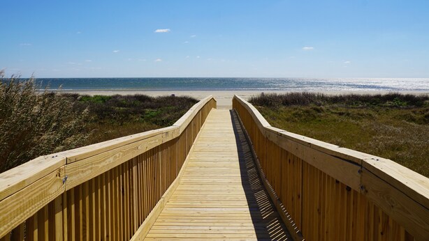 A wooden boardwalk leading to a beach with a clear sky.