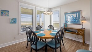 A dining area with a wooden table, six chairs, and a hanging light fixture.