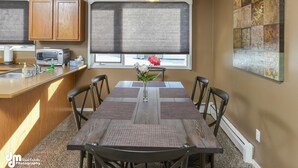 Una cocina con armarios de madera, microondas integrado y zona de comedor con mesa y sillas.