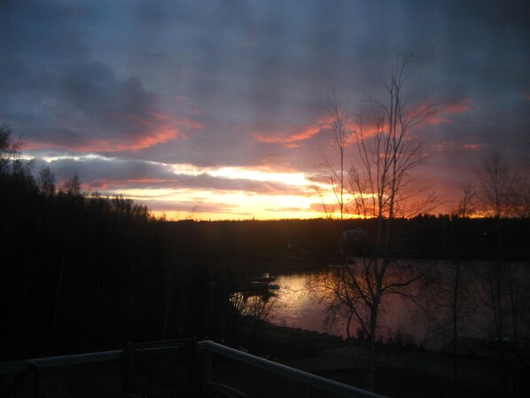 A sunset over a lake with a forested area in the foreground and a bridge in the lower left.