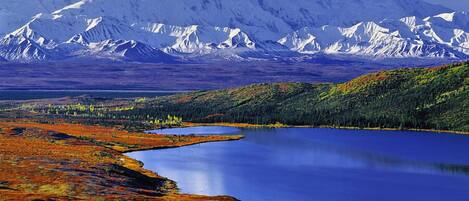 A lake surrounded by forested hills and a snow-capped mountain in the background.