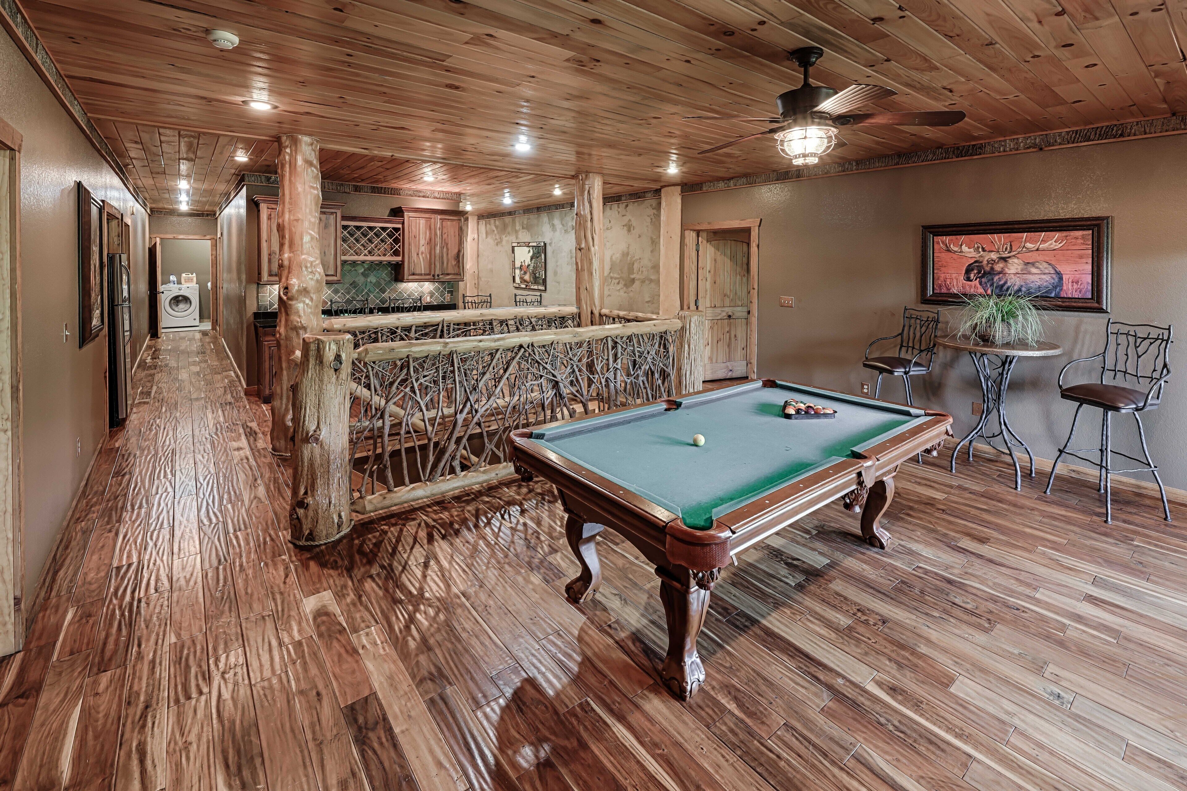 A wooden-floored room with a pool table, a bar area, and a dining table with chairs.